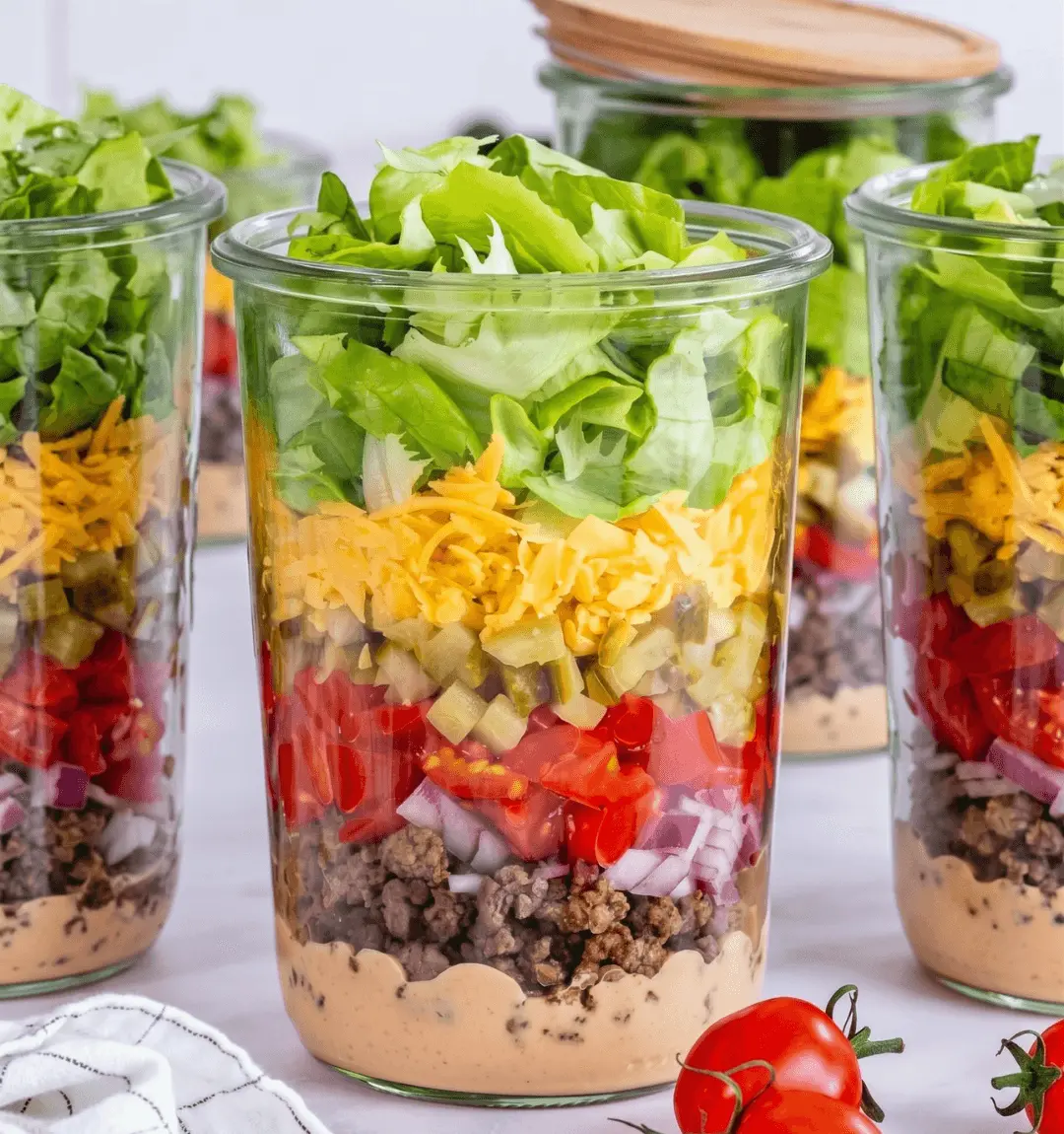 Ensalada en frasco estilo Big Mac con capas de aderezo, carne, tomate, pepinillos, queso cheddar y lechuga
